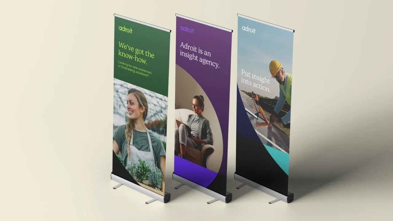 Three Adroit exhibition roller banners in the brand's purple, green and blue palette