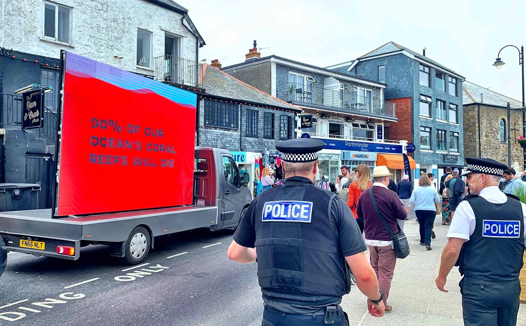 A mobile LED billboard van reading '90% of our ocean's coral reefs will die', watched by police on a Cornwall high street